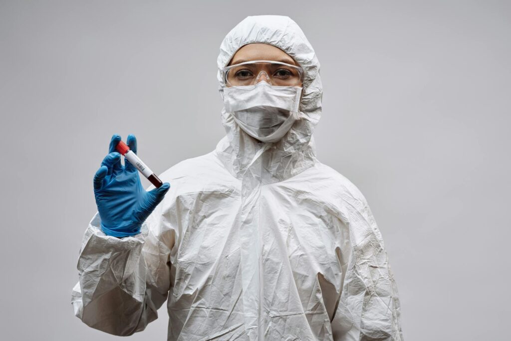 person in white coveralls and gloves holding a glass test tube